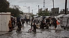 Heftiger Regen in Deir al-Balah. Palästinenser gehen durch eine überflutete Straße neben einem provisorischen Zeltlager.