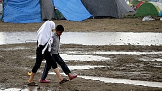 Children walk across a muddy filed at the northern Greek border point of Idomeni, Greece, Monday, April 25, 2016.