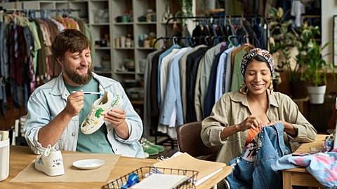A happy young man and woman sitting at a thrift store table and upcycling used denims and shoes. 