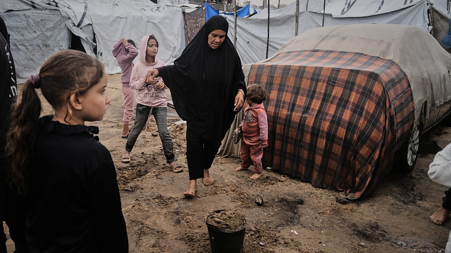 فلسطينيون نازحون يسيرون في الوحل داخل مخيم خيام مؤقت بعد هطول أمطار غزيرة في مدينة غزة يوم الثلاثاء 25 نوفمبر 2025. (تصوير: جيهاد الشريف/أسوشيتد برس)
