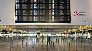 Pessoa atravessa o átrio vazio junto ao painel de partidas com voos cancelados no Aeroporto Internacional de Bruxelas
