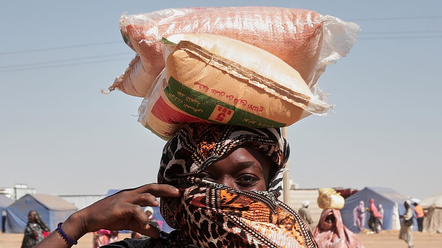 امرأة سودانية نازحة من الفاشر تحمل أكياس المساعدات الغذائية على رأسها في مخيم الإفاض الجديد في منطقة الدبة بولاية شمال السودان، يوم الأحد 16 نوفمبر 2025. (تصوير: مروان علي/أسو