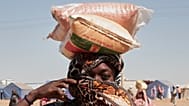 امرأة سودانية نازحة من الفاشر تحمل أكياس المساعدات الغذائية على رأسها في مخيم الإفاض الجديد في منطقة الدبة بولاية شمال السودان، يوم الأحد 16 نوفمبر 2025. (تصوير: مروان علي/أسو