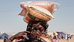 امرأة سودانية نازحة من الفاشر تحمل أكياس المساعدات الغذائية على رأسها في مخيم الإفاض الجديد في منطقة الدبة بولاية شمال السودان، يوم الأحد 16 نوفمبر 2025. (تصوير: مروان علي/أسو