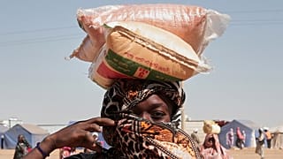 امرأة سودانية نازحة من الفاشر تحمل أكياس المساعدات الغذائية على رأسها في مخيم الإفاض الجديد في منطقة الدبة بولاية شمال السودان، يوم الأحد 16 نوفمبر 2025. (تصوير: مروان علي/أسو