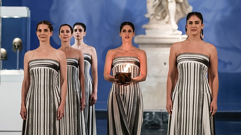 A főpapnő szerepét játszó Mary Mina görög színésznő a cserépedényben lévő olimpiai lángot tartja a kezében Olümpiában 2025. november 26-án