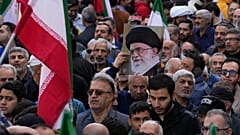 يحمل متظاهر لوحة للمرشد الأعلى الإيراني آية الله علي خامنئي بجانب أعلام إيران خلال التجمع السنوي أمام السفارة الأمريكية السابقة في طهران، احتفالًا بذكرى الاستيلاء على السفارة 