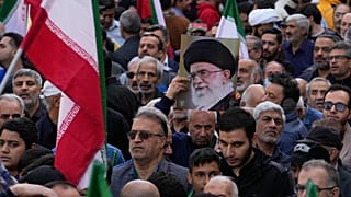 يحمل متظاهر لوحة للمرشد الأعلى الإيراني آية الله علي خامنئي بجانب أعلام إيران خلال التجمع السنوي أمام السفارة الأمريكية السابقة في طهران، احتفالًا بذكرى الاستيلاء على السفارة 