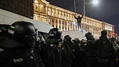 Manifestante em cima de um veículo da polícia enquanto milhares de pessoas tomam as ruas da capital da Bulgária, Sófia, para denunciar os impostos elevados previstos no orçamento do próximo ano, quarta-feira, 26 de novembro de 2025