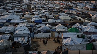 تجمّع فلسطينيون نازحون خارج خيمة في مخيم مؤقّت بمدينة دير البلح وسط قطاع غزة، يوم الأربعاء 26 نوفمبر/تشرين الثاني 2025. 