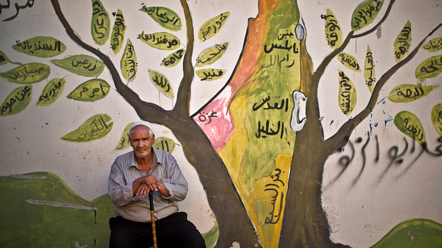 في هذه الصورة التي التُقطت يوم الثلاثاء 17 يونيو 2014، يظهر اللاجئ الفلسطيني علي أبو جبل، 73 عامًا، أمام جدار مرسوم عليه جداريّة تُصوّر أرض فلسطين