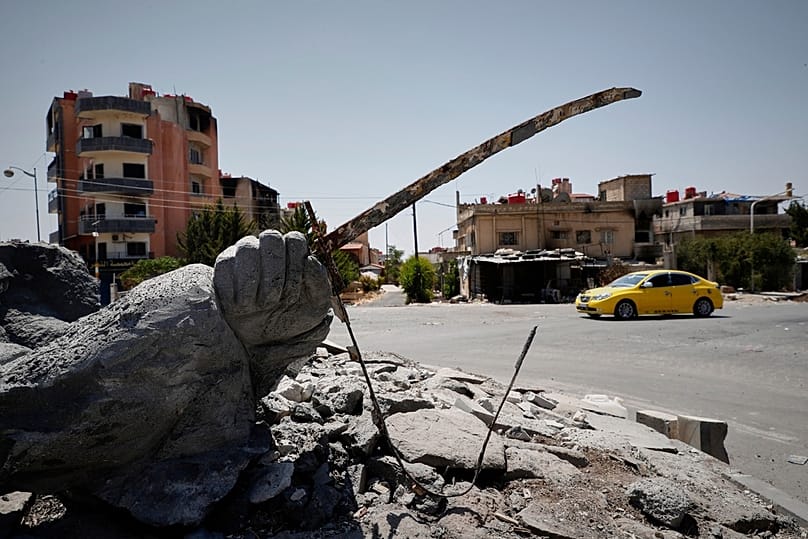 FILE - A car drives by a destroyed statue in the Druze-majority town of Suweyda, 25 July 2025.