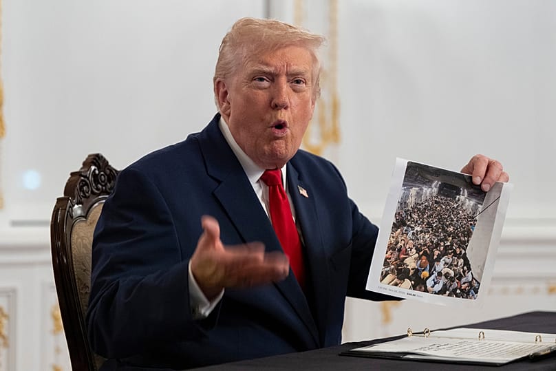 Trump holds up a photograph as he speaks to reporters after speaking to troops via video from his Mar-a-Lago estate on Thanksgiving, Thursday, Nov. 27, 2025, in Palm Beach