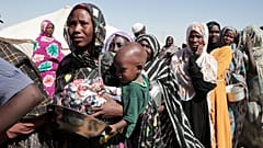 نساء سودانيات نازحات من الفاشر يقفن في طابور لتلقي مساعدات غذائية في مخيم العفاد الذي أُنشئ حديثًا في الدبة، بولاية شمال السودان، 
