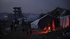 يقف فلسطينيون نازحون قرب نار أوقدوها بجانب خيمتهم وسط الدمار الذي خلّفته العملية الجوية والبرية في مدينة غزة، الجمعة 28 نوفمبر/تشرين الثاني 2025. (أ ب / عبد الكريم هنا)