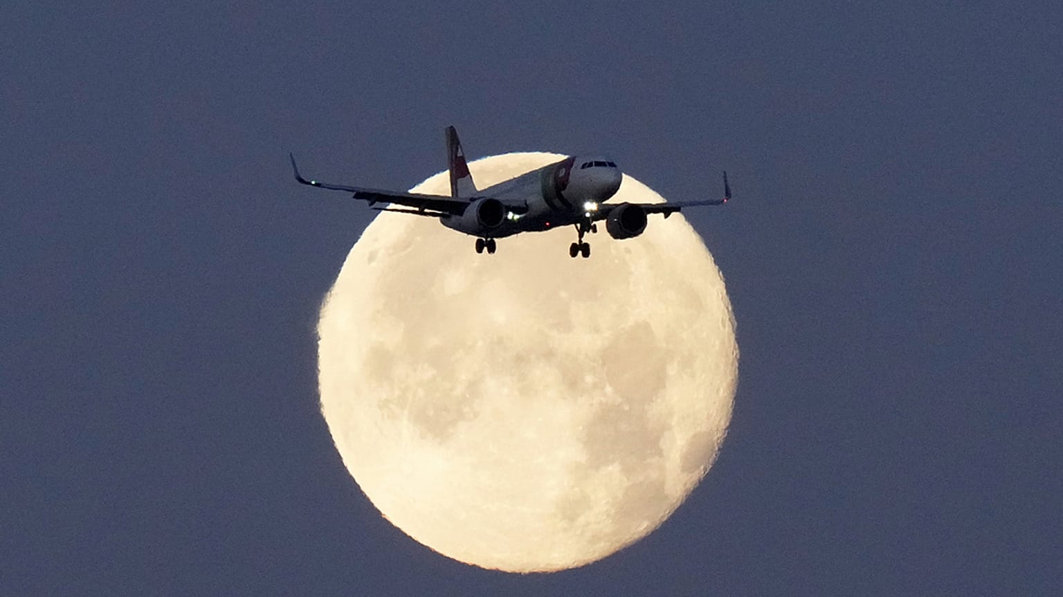 A TAP Air Portugal Airbus A320 is silhouetted against the setting moon while approaching for landing in Lisbon, Portugal, June 23, 2024. 
