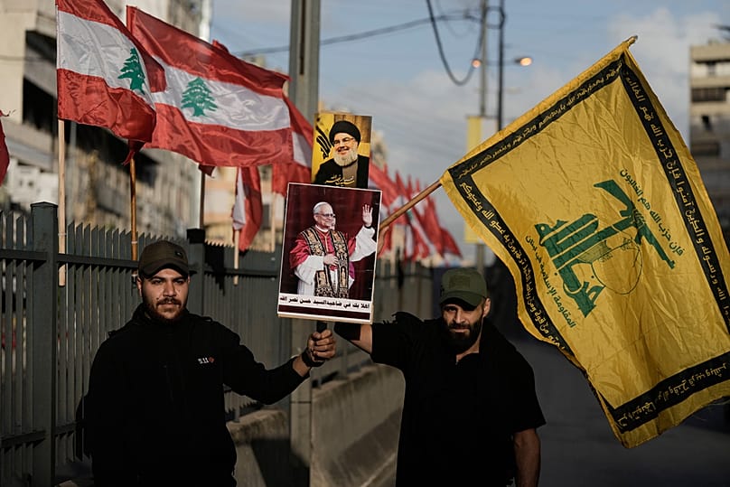 كشافة المهدي التابعة لحزب الله تحمل صور نصر الله وأعلام الحزب أثناء استقبالهم البابا ليو الرابع عشر والرئيس عون عند وصولهما إلى مطار بيروت.