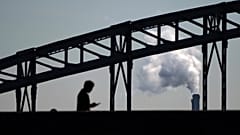 Un homme regarde son téléphone en marchant sur un pont, avec en arrière-plan la fumée d'un incinérateur de déchets, en périphérie de Paris, jeudi 23 septembre 2021.