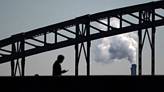 A man looks his phone while walking on a bridge with the smoke of a waste incinerator in background on the outskirts of Paris, Thursday, Sept. 23, 2021. 