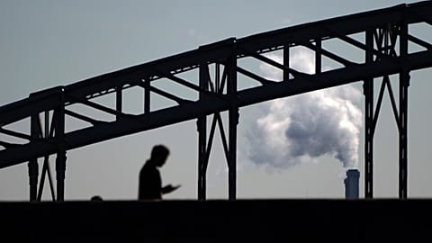 A man looks his phone while walking on a bridge with the smoke of a waste incinerator in background on the outskirts of Paris, Thursday, Sept. 23, 2021. 