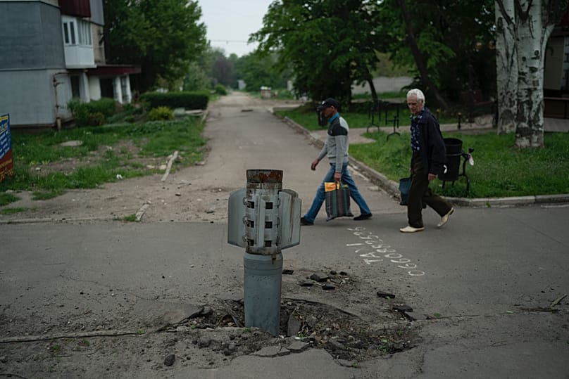 FILE - People walk past part of a rocket that sits wedged in the ground in Lysychansk, Luhansk region, Ukraine, Friday, May 13, 2022. 