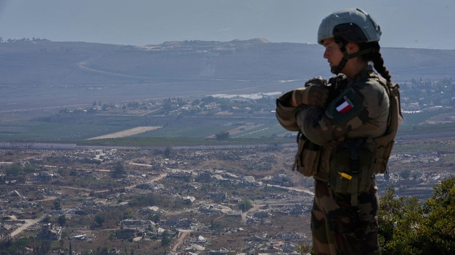 جندية فرنسية من قوات الأمم المتحدة تقف على تلة مطلّة على بلدة كفركلا الحدودية، التي دمّرتها الغارات الجوية والهجوم البري الإسرائيلي، في جنوب لبنان، 20 آب 2025.