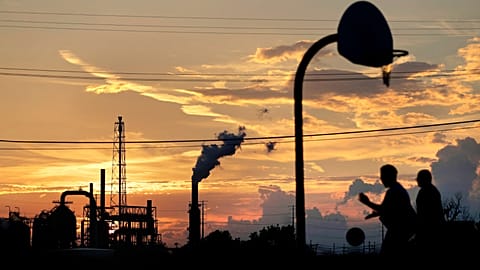 An oil refinery stands in the background as children play on a basketball court in Port Arthur, Texas, Wednesday, Sept. 27, 2017. 