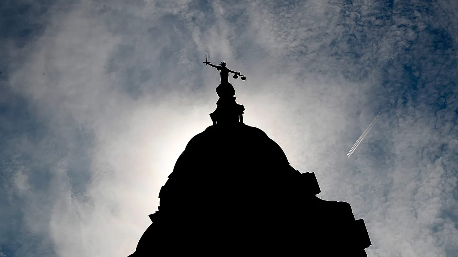 A statue of liberty is silhouetted as it sits on top of the Old Bailey in London, 8 August, 2019