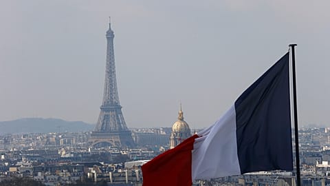  Un drapeau français flotte sur l'horizon de la capitale française, avec la Tour Eiffel, le dôme des Invalides et les toits des immeubles vus depuis les colonnes du dôme du Panthéon à Paris, France.