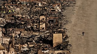 Una persona camina por la playa junto a viviendas dañadas por el incendio de Palisades, el 16 de enero de 2025, en Malibú.