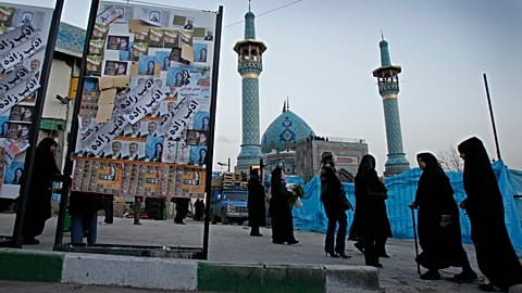 يمرّ إيرانيون بجانب ملصق انتخابي مغطى بملصقات لمرشحين مختلفين قبل يومين من الانتخابات البرلمانية الإيرانية، يوم الأربعاء 29 فبراير/شباط 2012، في شمال طهران. 