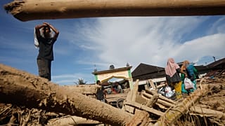 Выжившие проходят мимо бревен, унесенных внезапным паводком, в Батанг-Тору, Северная Суматра, Индонезия.