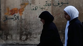 Kobiety przechodzą obok muru z graffiti z napisem w języku arabskim „Zostaniemy tutaj, Assad” w mieście Homs w Syrii, piątek, 21 listopada 2025 r. (AP Photo/Omar Sanadiki)