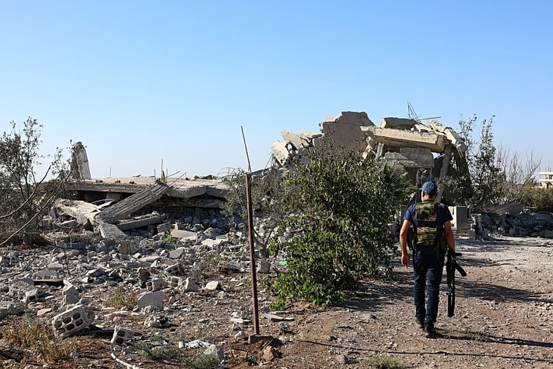 A gunman walks by the remains of a house destroyed during the recent sectarian clashes in the Druze-majority town of Suweyda, 19 September 2025. 