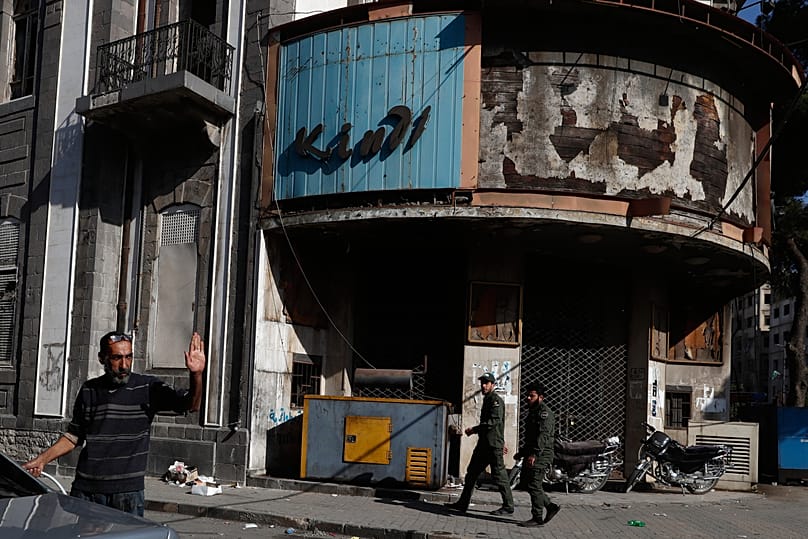 Syrian army fighters walk past an abandoned cinema in downtown Homs, 21 November, 2025