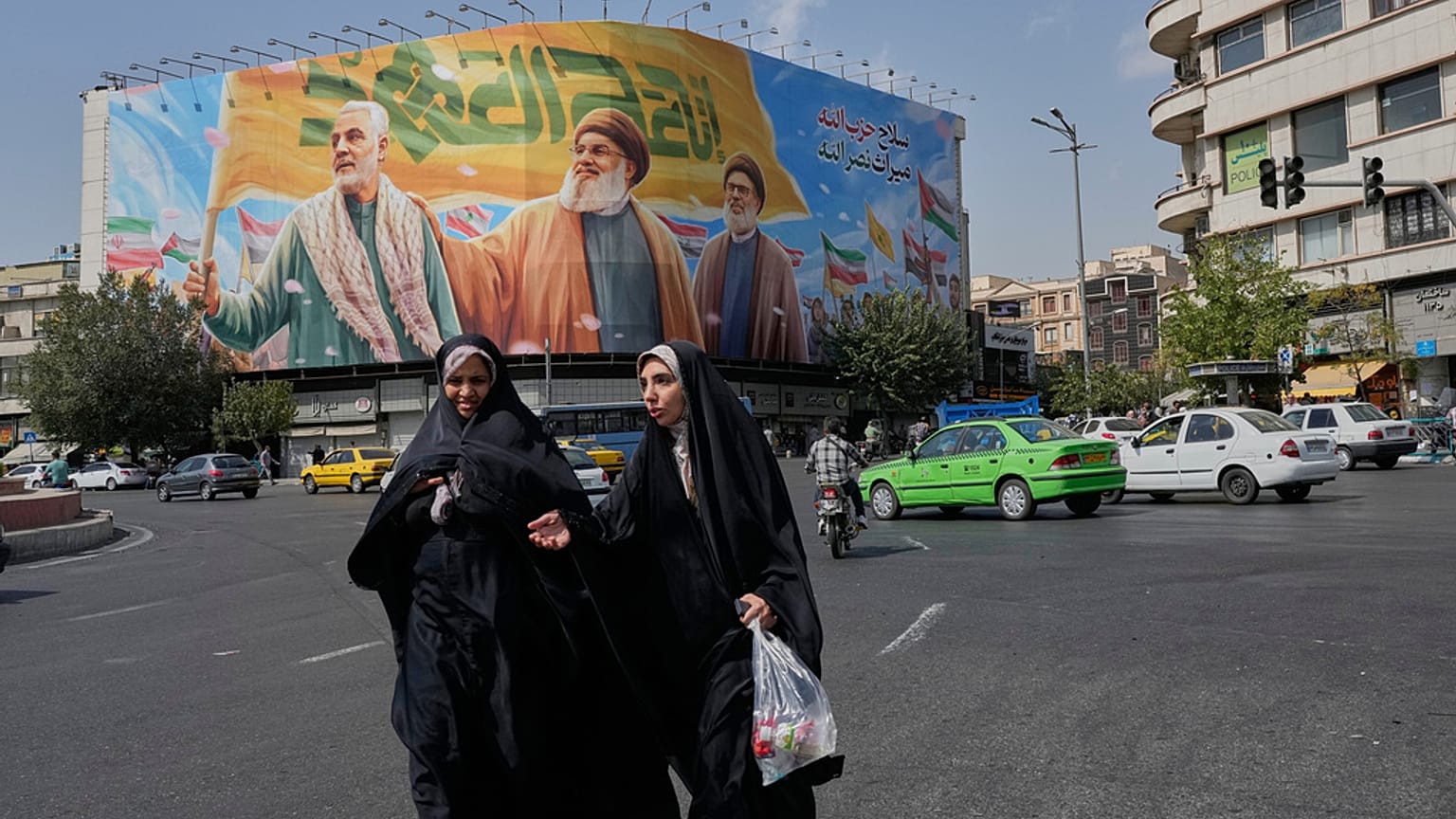 امرأتان تمشيان بالقرب من لوحة ضخمة تضم قاسم سليماني وحسن نصر الله وهاشم صفي الدين، طهران، السبت 27 سبتمبر 2025