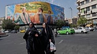 امرأتان تمشيان بالقرب من لوحة ضخمة تضم قاسم سليماني وحسن نصر الله وهاشم صفي الدين، طهران، السبت 27 سبتمبر 2025