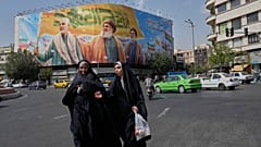 امرأتان تمشيان بالقرب من لوحة ضخمة تضم قاسم سليماني وحسن نصر الله وهاشم صفي الدين، طهران، السبت 27 سبتمبر 2025