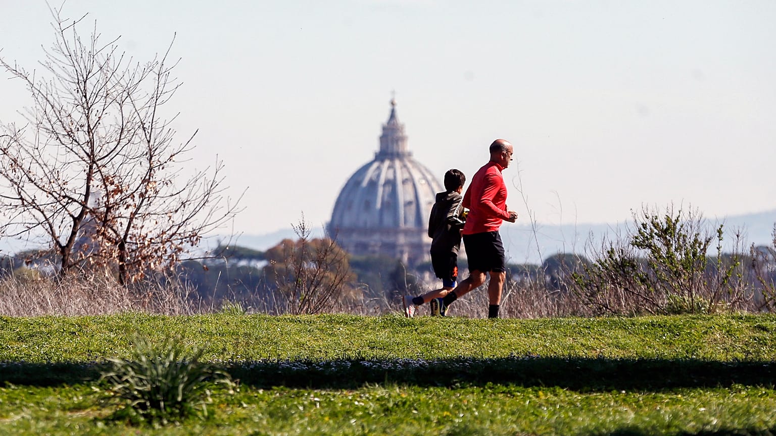 يظهر الناس وخلفيتهم قبة كاتدرائية القديس بطرس بينما يمارسون الرياضة في حديقة في روما، الأربعاء، 11 مارس 2020. (سيسيليا فابيانو/لا بريس عبر AP)