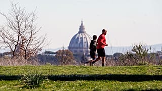 يظهر الناس وخلفيتهم قبة كاتدرائية القديس بطرس بينما يمارسون الرياضة في حديقة في روما، الأربعاء، 11 مارس 2020. (سيسيليا فابيانو/لا بريس عبر AP)