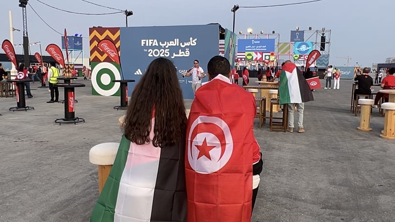 A Tunisian and a Palestinian fan sit together at the Lusail Boulevard fan zone.