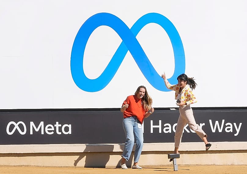 A Facebook-alkalmazottak az új Meta logó előtt fényképezkednek, 2021. október 28-án