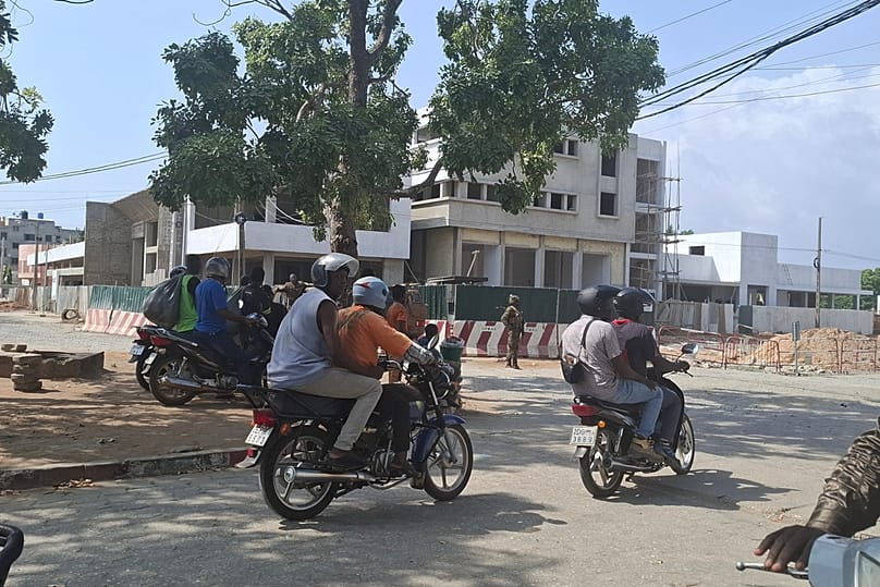 Des motards passent devant des soldats gardant une rue lors d'une tentative de coup d'État dans la capitale béninoise Cotonou, dimanche 7 décembre 2025.