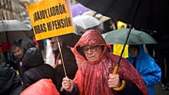 Un hombre con una pancarta en la que se lee en español: "Rajoy ladrón, me robaste la pensión" camina bajo la lluvia durante una protesta de pensionistas en Madrid. 17 de marzo de 2018.