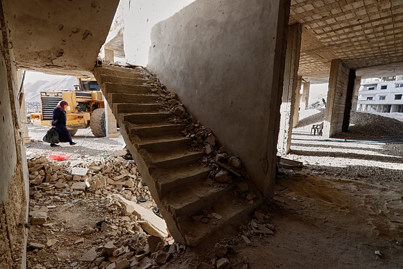 امرأة تمرّ بجانب مبنى تضرّر جراء الحرب في ضاحية داريا بدمشق، سوريا، يوم الجمعة 5 كانون الأول/ديسمبر 2025. 