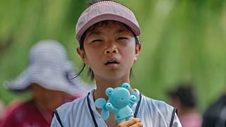 A child holds an electric fan as they react to the heat during a visit to the Forbidden City in Beijing, July 8, 2024.