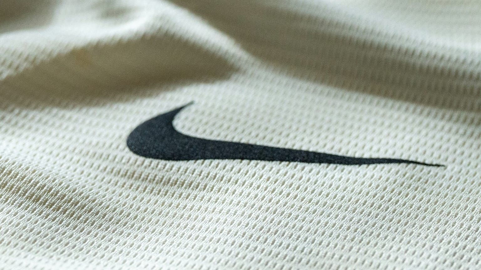 Il celebre logo Swoosh di Nike appare su un tessuto color crema.