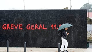 Image de l'article  Portugal   Retour  Importer Grève générale au Portugal  Une femme passe devant un graffiti où l'on peut lire « Greve Geral » (grève générale)
