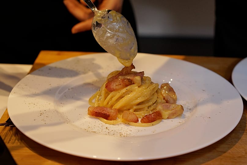 A creamy mix of grated pecorino cheese and egg drops from a spoon in Rome during Carbonara Day