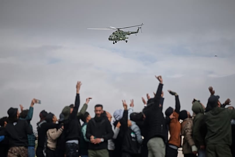 Ein Armeehubschrauber fliegt während einer Parade der neuen syrischen Armee über Männern, die den ersten Jahrestag des Sturzes des Bashar-al-Assad-Regimes in Damaskus feiern, 